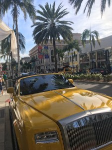 A yellow car parked on a street with palm trees.