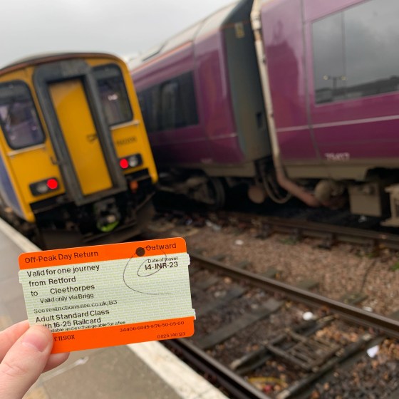 A paper ticket is held in someone's hand, in front of two train carriages.